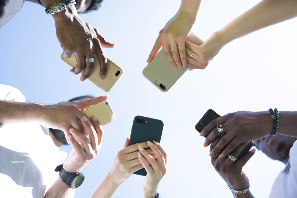 Group of people holding up their phones together, seen from below against the sky