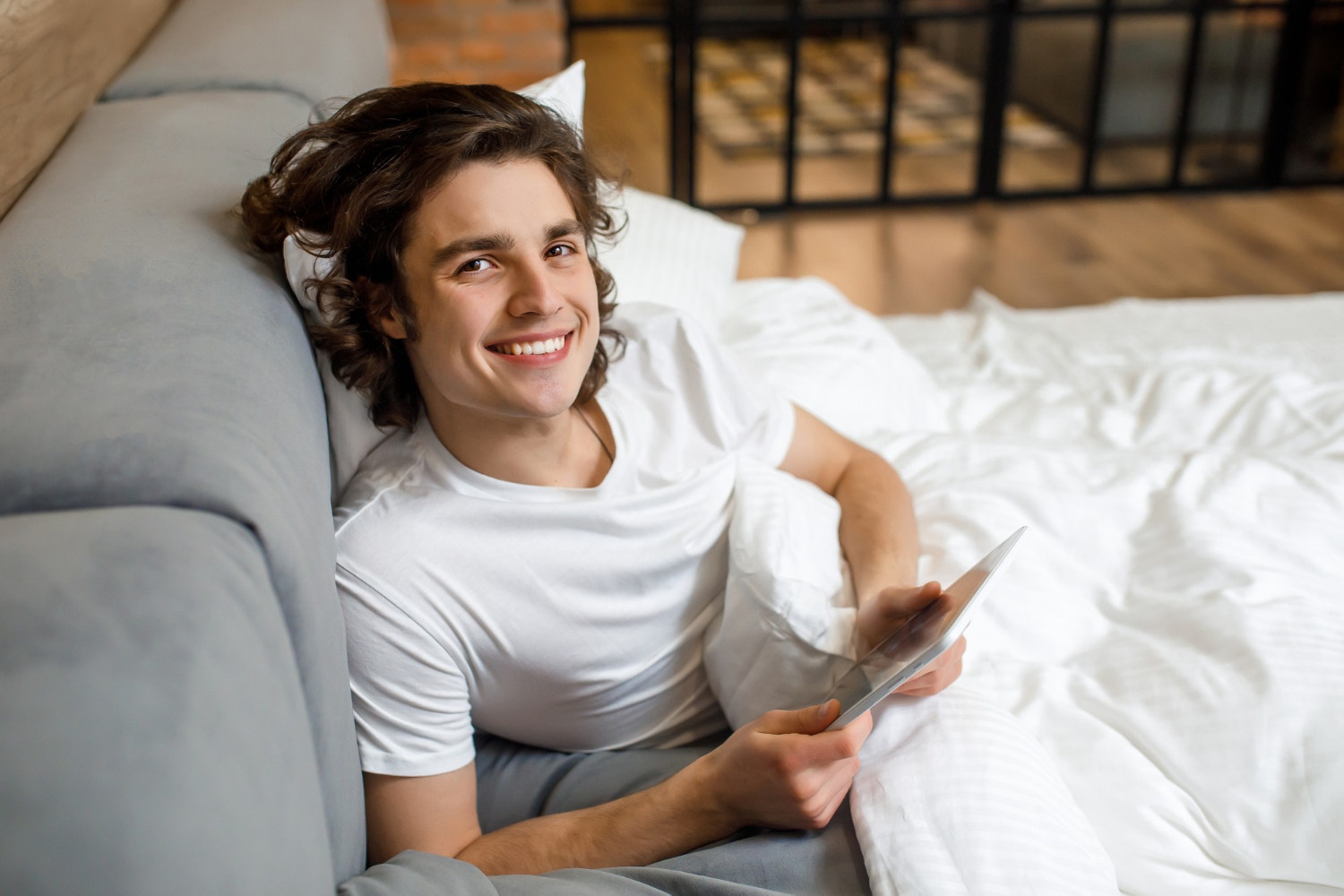 Smiling young man relaxing in bed using a tablet