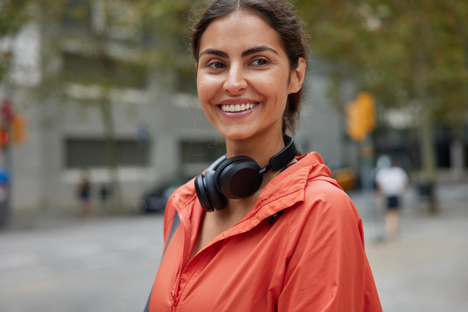 Smiling woman with headphones around her neck standing outside in the city