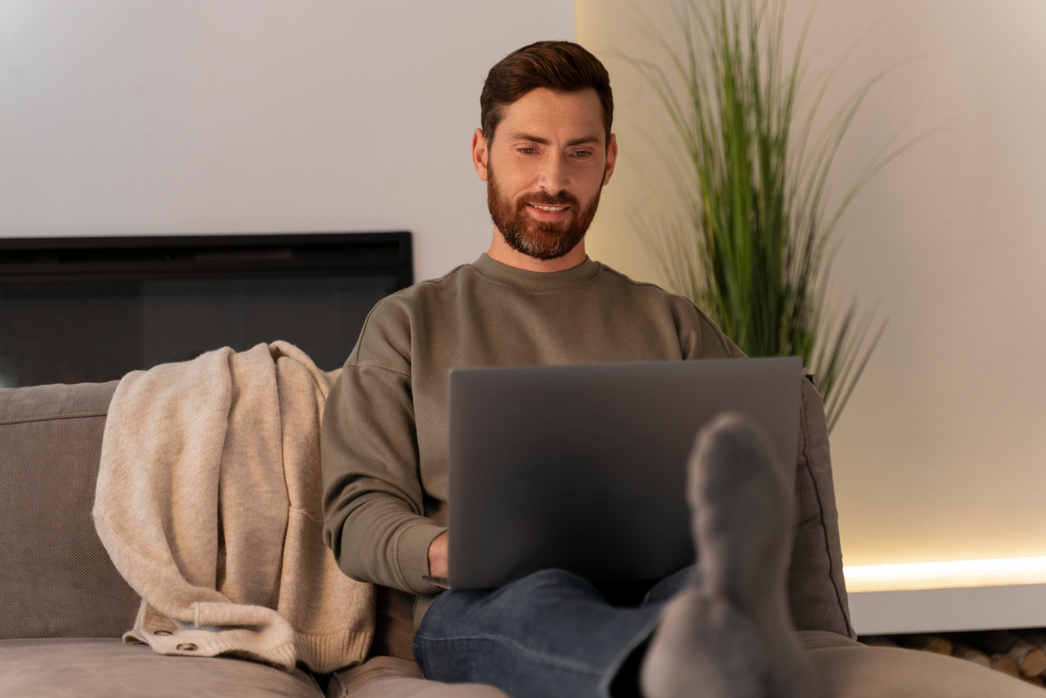 Man relaxing on a couch smiling while on a video chat on his laptop