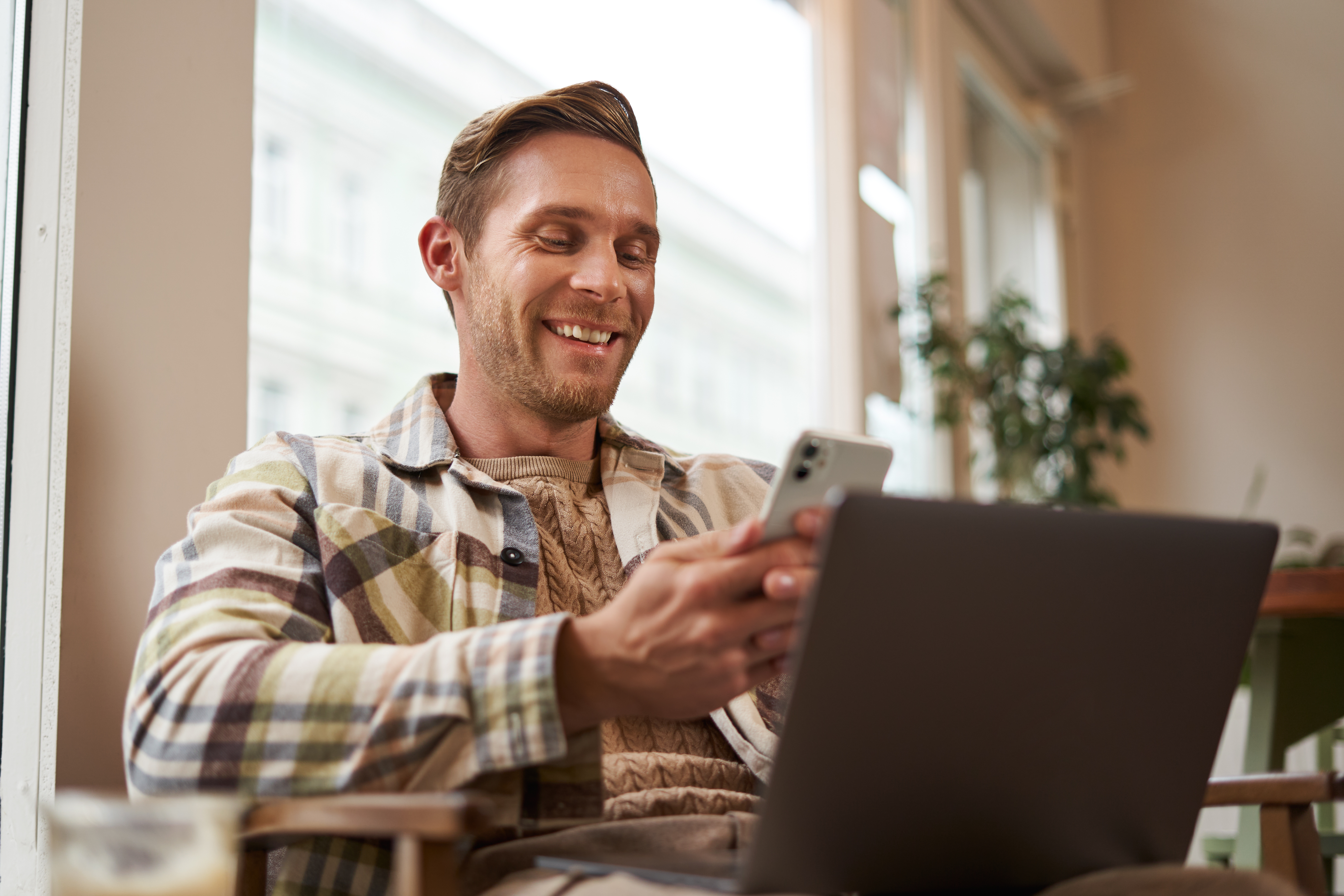 Smiling man with laptop and smartphone at a café
