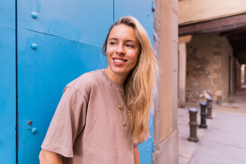 Smiling woman with long blonde hair leaning against a blue door on a city street