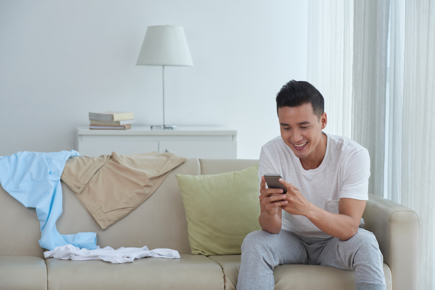 Smiling man sitting on a couch at home laughing while looking at his phone