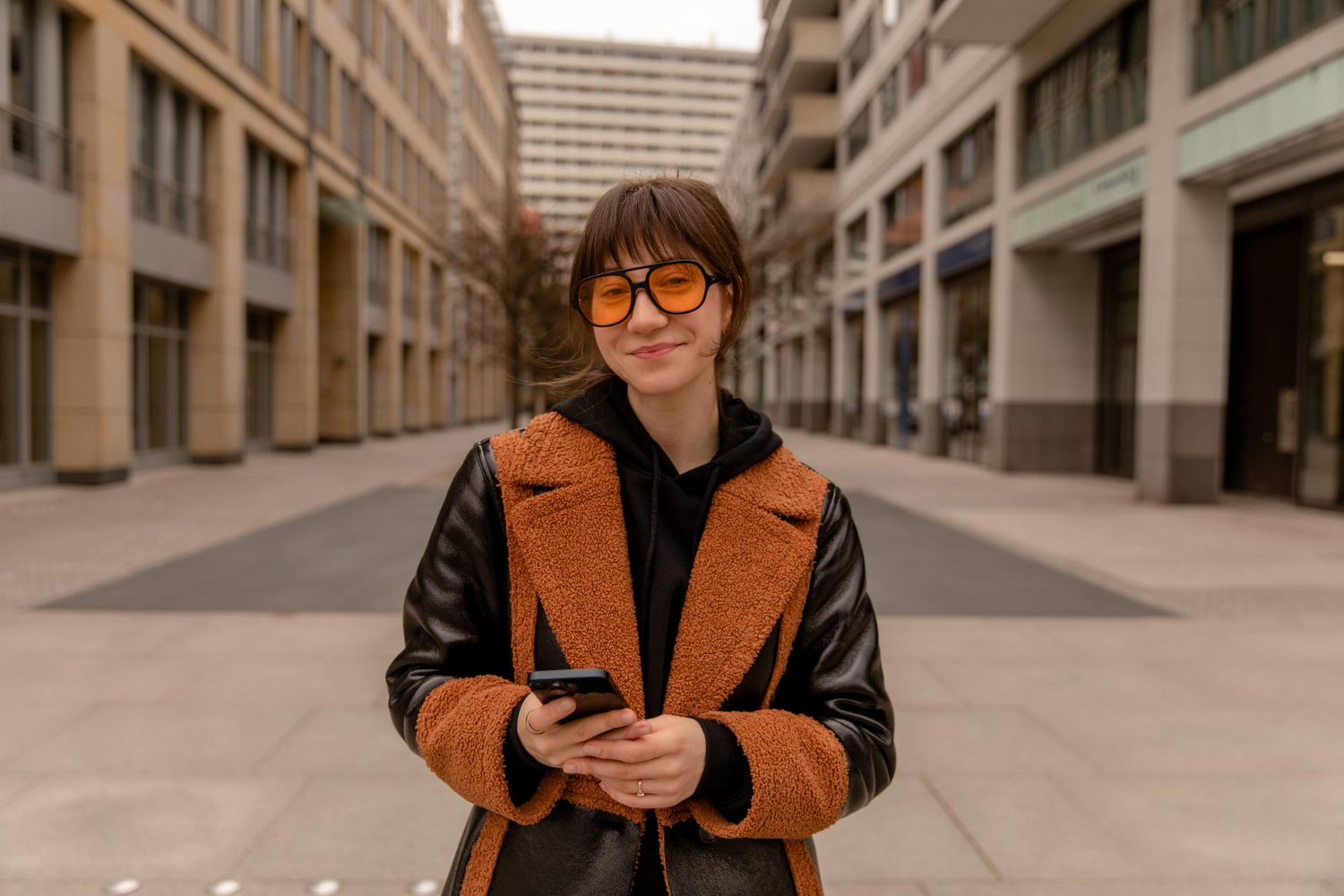 Smiling woman in sunglasses holding her phone on a city street