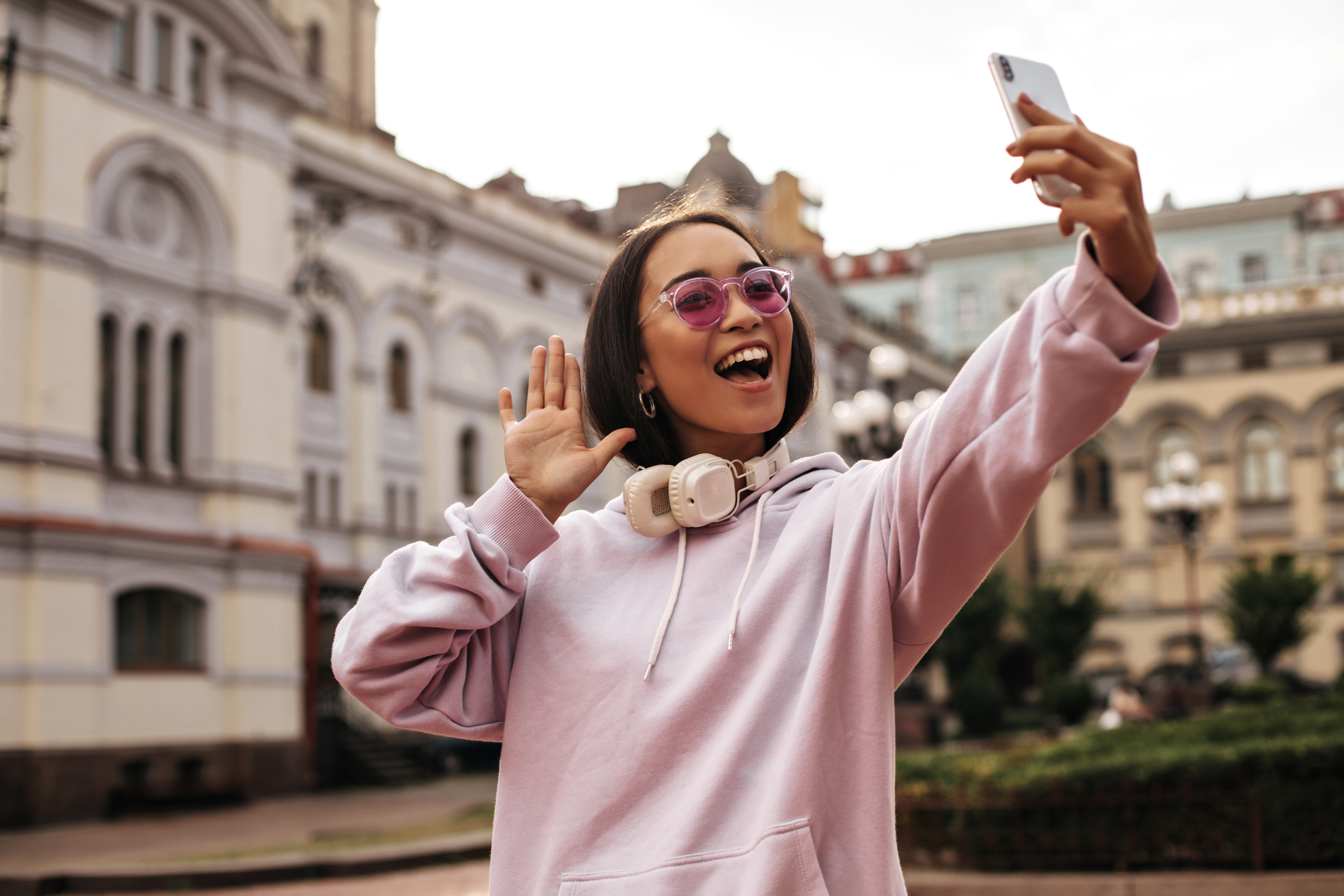 Young woman in pink hoodie with sunglasses taking a selfie outdoors